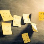Yellow sticky notes on black board below "Customer satisfaction" word. The notes have smiles drawn with a black color marker to represent the happy clients